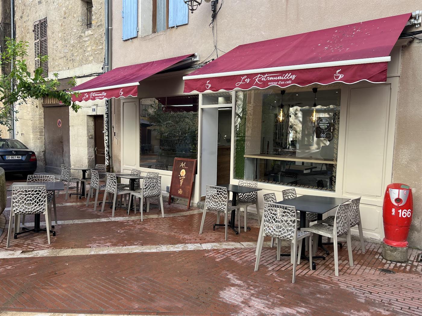 Façade des Retrouvailles avec son store bordeaux et ses tables en terrasse