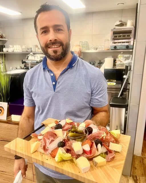 Le patron des Retrouvailles, sourire aux lèvres, tenant une grande planche de charcuterie et de fromages