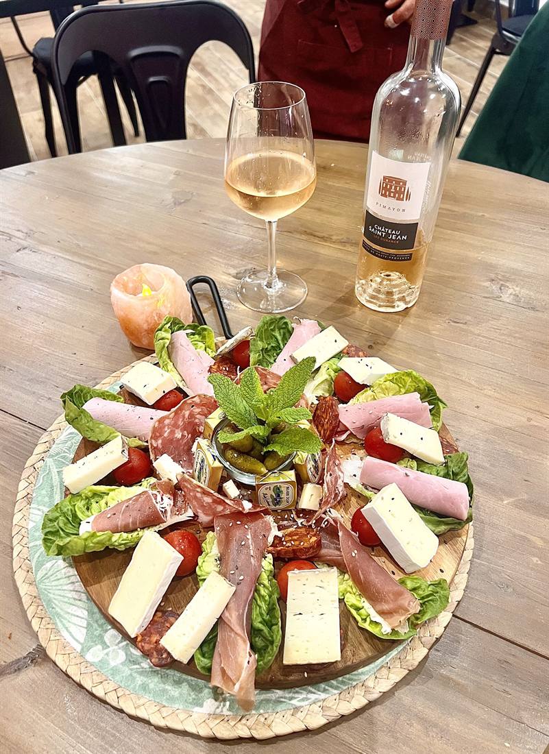 Planche de charcuterie, fromages et salade posée à côté d'un verre de vin rosé