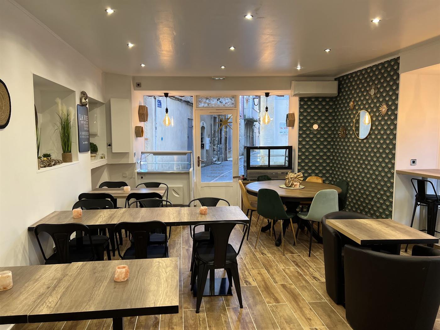 Salle des Retrouvailles : tables en bois, chaises noires et grandes baies vitrées