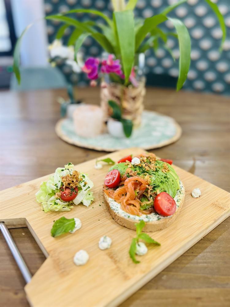 Tartine de saumon et avocat sur une planche en bois, avec une plante en décor